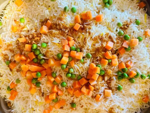 A close-up of fluffy white rice mixed with green peas and diced carrots, topped with crispy fried onions.