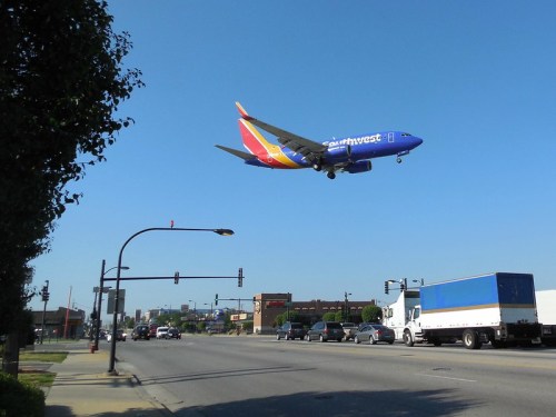 A Southwest Airlines plane approaches landing over a busy street with vehicles and traffic signals below.