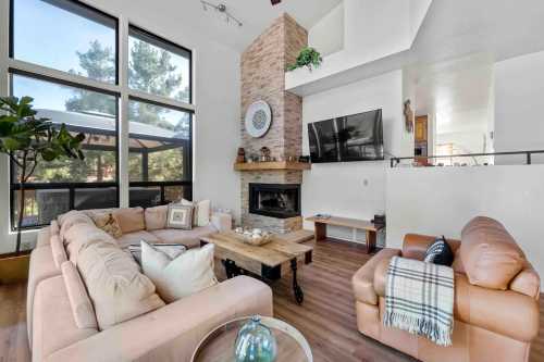 Cozy living room with a stone fireplace, large windows, and comfortable seating, featuring a modern design and warm decor.