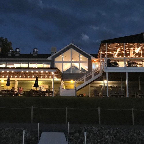 A cozy restaurant with outdoor seating, illuminated at night under a cloudy sky.
