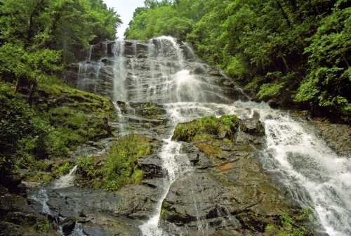 A cascading waterfall flows down rocky terrain, surrounded by lush green trees and foliage.