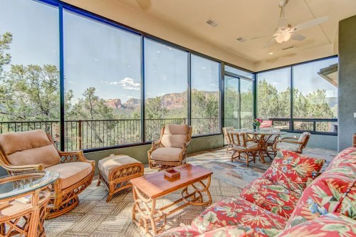 A cozy sunroom with floral furniture, large windows, and a view of trees and mountains in the background.