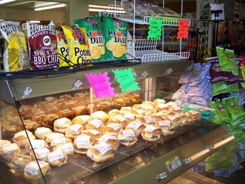 A display case filled with sandwiches and a variety of snack bags on shelves in a store. Brightly colored signs are visible.