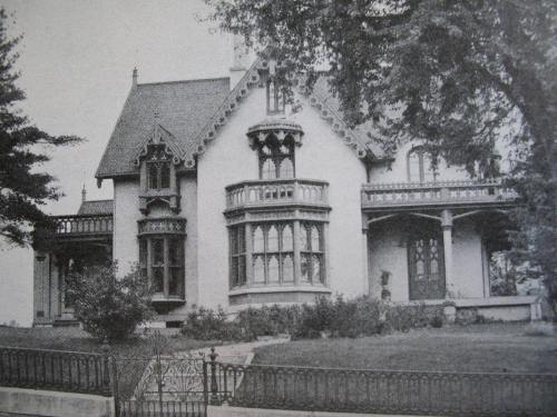 A vintage black-and-white photo of a large, ornate Victorian-style house with intricate architectural details.