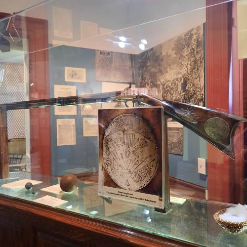 A display case featuring a historical artifact, a book with an engraved cover, and various documents in a museum setting.