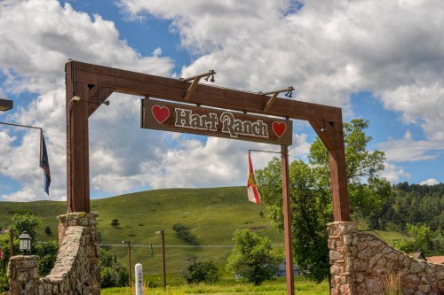 Sign for Hart Ranch with a heart design, set against a backdrop of green hills and a blue sky with clouds.