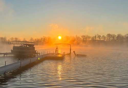 A serene sunrise over a misty lake, with a dock and boat silhouetted against the golden sky.