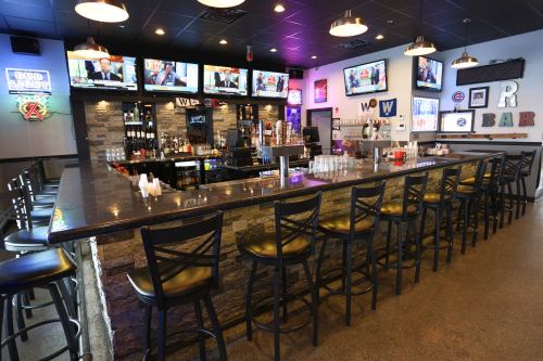 A modern bar with a stone counter, empty stools, and multiple TVs displaying sports in a vibrant setting.