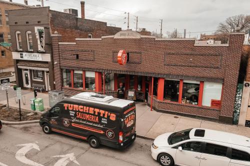 A street view of Turchetti's Salumeria with a food truck parked outside and nearby shops in a city setting.
