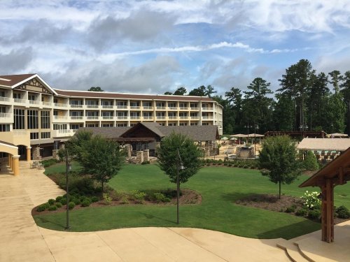 A spacious resort with a large lawn, trees, and a pool area, set against a backdrop of cloudy skies.