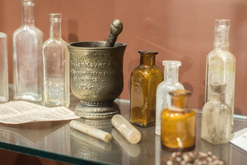 A collection of vintage glass bottles and a metal mortar and pestle displayed on a glass shelf.