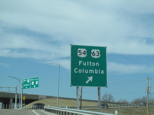 Green highway sign indicating routes 54 and 63 to Fulton and Columbia, with an arrow pointing right.