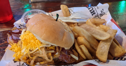 A burger topped with cheese and bacon, served with a side of golden fries on a paper-lined tray.