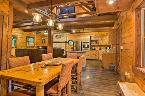 Cozy wooden cabin interior featuring a dining table, kitchen, and warm lighting. Rustic decor enhances the inviting atmosphere.