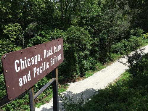 Sign for the Chicago, Rock Island and Pacific Railroad overlooking a gravel path surrounded by lush greenery.