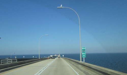 A highway bridge stretches over water, with a clear blue sky and a mile marker sign visible on the right.