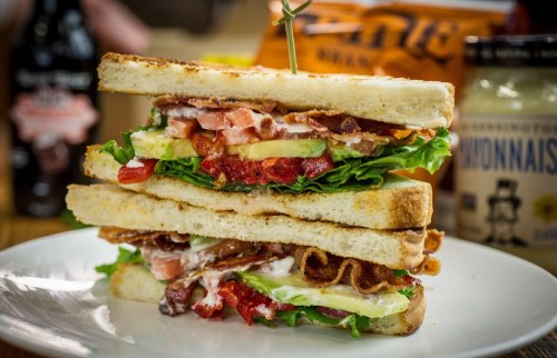 A stacked sandwich with bacon, lettuce, tomato, and mayonnaise, served on toasted bread with condiments in the background.