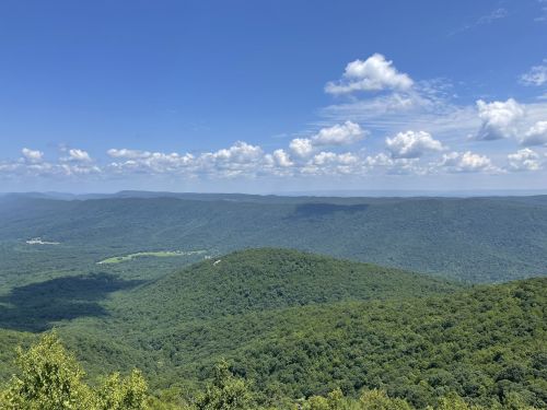 A panoramic view of lush green mountains under a bright blue sky with scattered clouds.