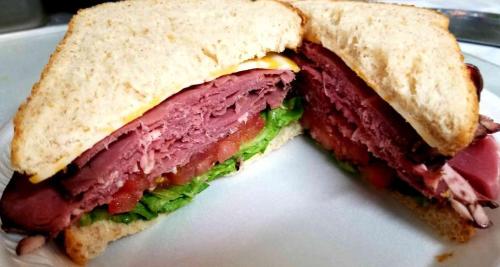 A close-up of a sandwich with layers of roast beef, lettuce, tomato, and cheese between two slices of whole grain bread.
