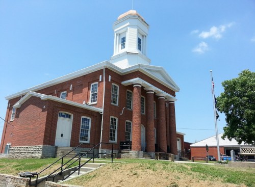 Historic brick building with a white cupola, columns, and a flagpole, set against a clear blue sky.