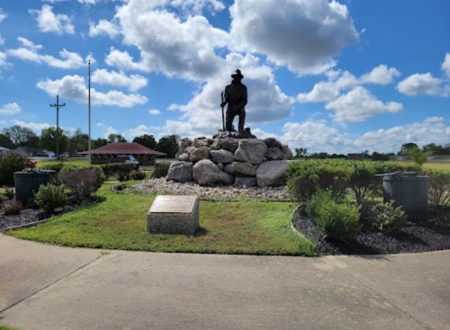 A statue of a man on a rock pedestal surrounded by greenery and clouds in a blue sky.