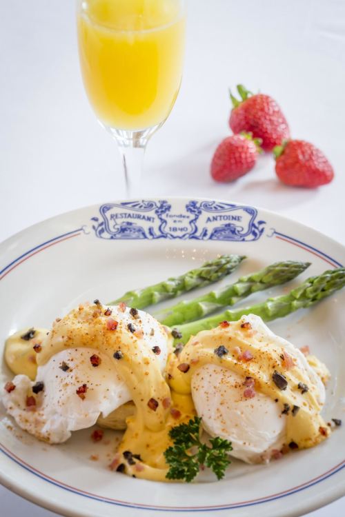 A plate of poached eggs with hollandaise sauce, asparagus, and a mimosa, garnished with strawberries.