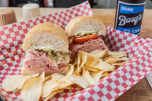 A basket with two sandwiches filled with deli meats, lettuce, and tomato, served with a side of potato chips.