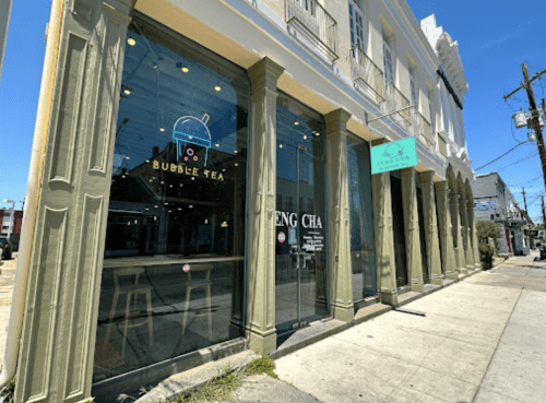 Exterior of a bubble tea shop with large glass windows and a colorful sign, set against a clear blue sky.