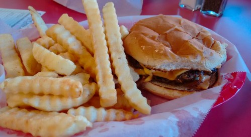 A plate with a cheeseburger and a side of crinkle-cut fries on a red table.