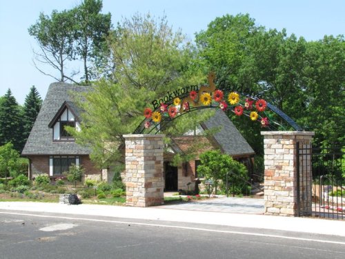 A charming stone archway adorned with flowers leads to a picturesque house surrounded by lush greenery.