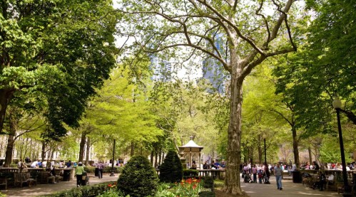 A vibrant park scene with lush green trees, people enjoying the outdoors, and a gazebo in the background.
