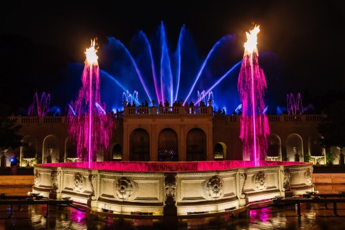 A vibrant fountain display at night, featuring colorful lights and water jets shooting up against a dark sky.