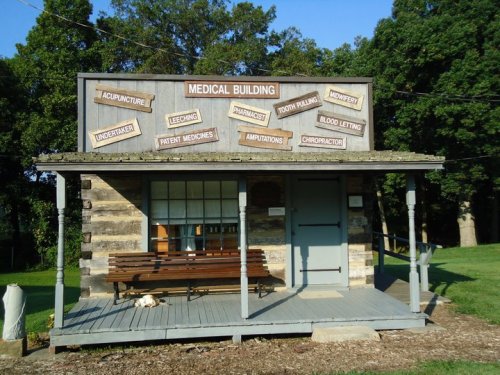 A rustic medical building with a sign listing various treatments, surrounded by trees and a grassy area.