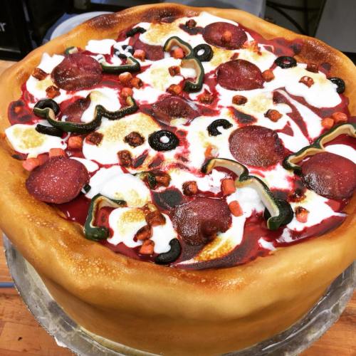 A large, realistic cake designed to look like a pepperoni pizza, complete with toppings and a golden crust.