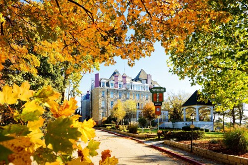 Historic building surrounded by vibrant autumn leaves and a clear blue sky. A gazebo is visible in the background.