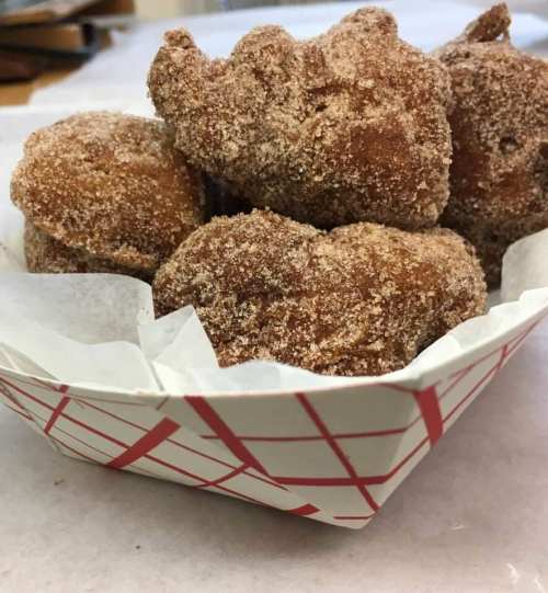 A basket of cinnamon-sugar coated fried dough balls, arranged neatly with a white paper liner.