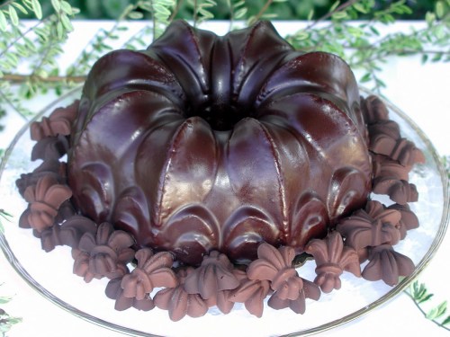 A rich chocolate bundt cake adorned with chocolate flower decorations on a glass platter.