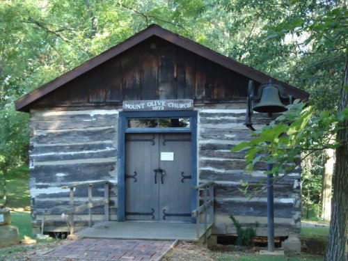 A rustic log cabin church with a bell, surrounded by trees, marked "Mount Olive Church 1873."