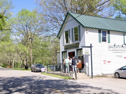 A white building with a green roof, labeled "Wallace Station," with people entering and trees in the background.