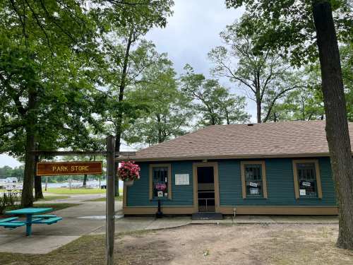 A blue park store with a brown roof, surrounded by trees, featuring a sign and flower baskets.