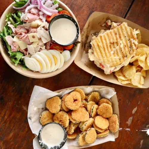 A bowl of salad with turkey, cheese, and eggs, a sandwich with chips, and a plate of fried snacks with dipping sauce.