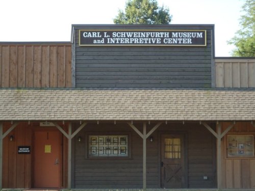 Exterior of the Carl L. Schweinfurth Museum and Interpretive Center, featuring wooden architecture and a sign.