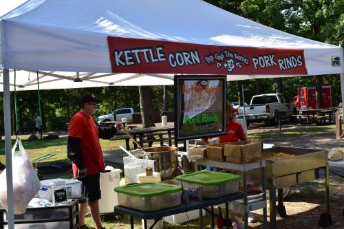 A food stall with a sign for kettle corn and pork rinds, featuring two staff members in red shirts.