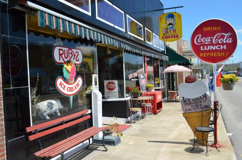 A charming ice cream shop with colorful signage, outdoor seating, and a large ice cream cone display on the sidewalk.