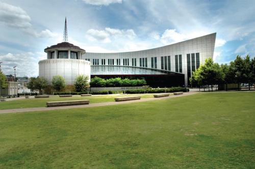 Modern building with a curved design, surrounded by green grass and trees under a partly cloudy sky.