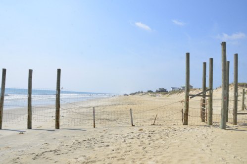 A sandy beach with wooden posts and a net, stretching towards the ocean under a clear blue sky.