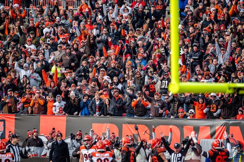 A lively crowd of fans in orange and brown jerseys cheers enthusiastically at a football game.