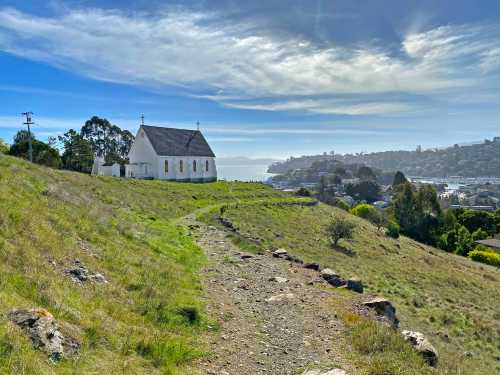 A white church on a hillside with a scenic view of a bay and distant hills under a blue sky.