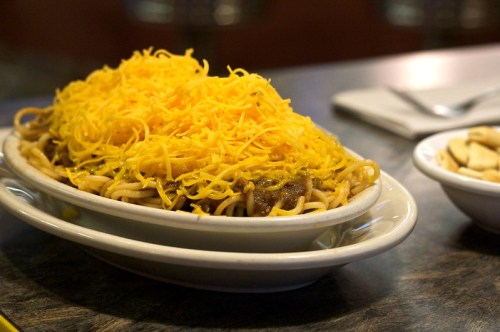A bowl of spaghetti topped with a generous layer of shredded cheese, served alongside a small dish of crackers.