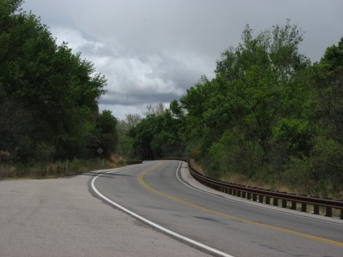 A winding road surrounded by lush green trees under a cloudy sky.